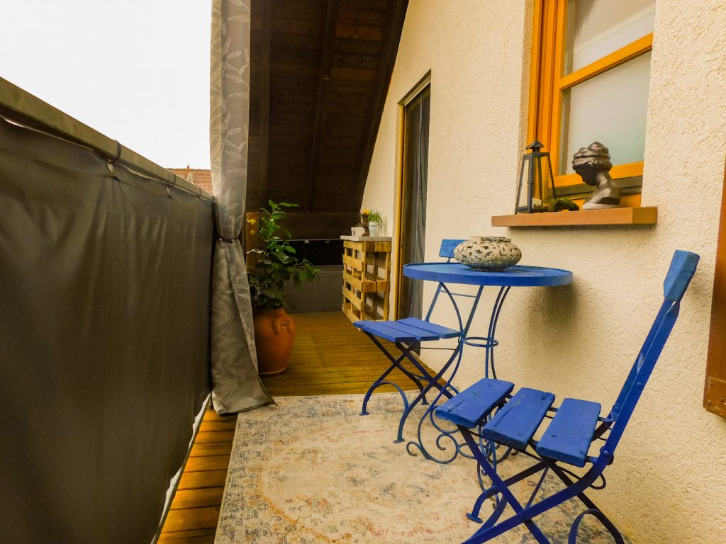 Balkon von der anderen Seite: Tisch und zwei Stühle, Deko, Outdoor-Vorhänge als Sichtschutz