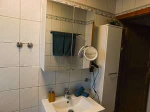 Blick von der Badewanne aus auf Waschbecken mit Spiegelschrank und einem weiteren Schrank rechts vom Waschbecken
